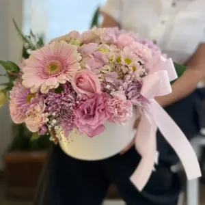 Arreglo Bonita con flores rosadas en base cilíndrica blanca.