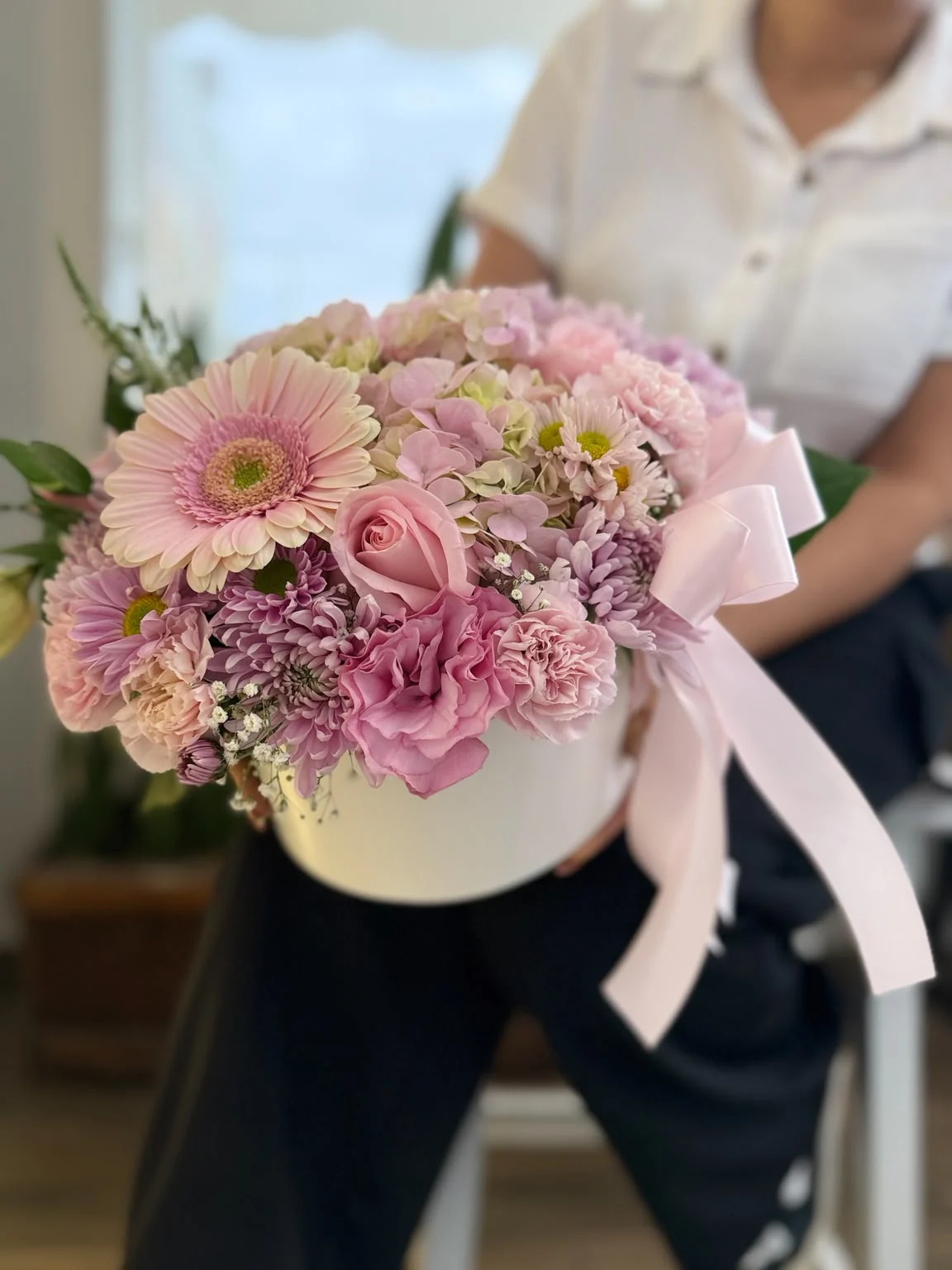 Arreglo Bonita con flores rosadas en base cilíndrica blanca.